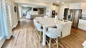 A modern kitchen with white cabinetry, a stainless steel refrigerator, and a dining area with a white table and chairs. - Massive Lakehouse - Infinity Pool, Hot Tubs, Dock, Firepit (Gainesville)
