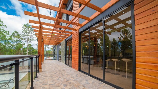 Ein überdachter Außenbereich mit einer Holzw pergola, Glastüren und einem gefliesten Boden.