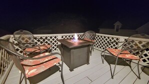 A deck with a table and two chairs, a fire feature, and a lattice railing. - Downtown home blocks to the beach w/ king bed, deck fire pit & air conditioning (Manistee)