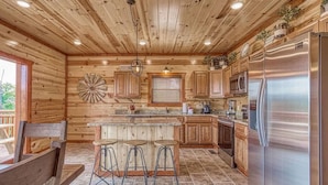 Una cocina con paredes de madera, un refrigerador de acero inoxidable y taburetes de bar.