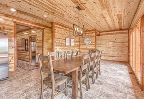A wooden interior with a dining table, chairs, a clock, and a refrigerator.