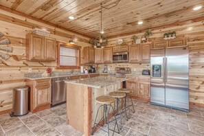 A kitchen with wooden cabinets, a stainless steel refrigerator, a granite countertop, and a bar stool area.