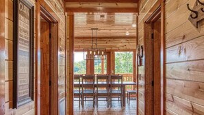 Interior de una cabaña de madera con comedor, una araña y vistas al exterior.