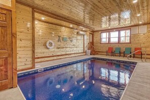 An indoor swimming pool with wooden walls, a lifebuoy, and a set of stairs leading to a window.