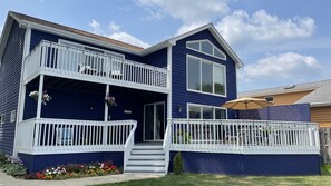 Uma casa de dois andares com uma varanda no primeiro andar, um pequeno alpendre frontal e uma placa com a inscrição 'Beach House'.