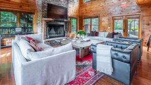 L’intérieur d’une cabane en rondins, avec une cheminée en pierre, des murs en bois et de grandes fenêtres.