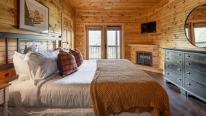 Une chambre dans une cabane en bois, comprenant un lit, une commode, une cheminée et un ventilateur de plafond.