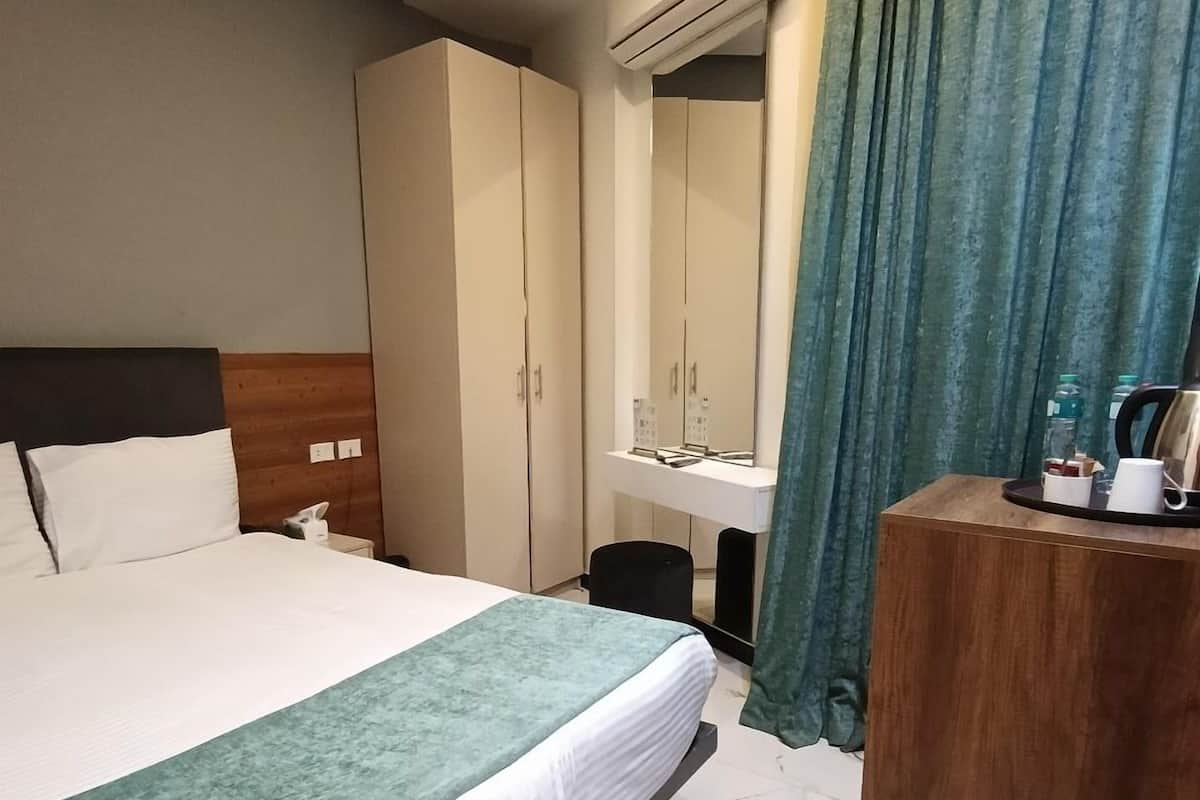 A hotel room with a bed, a wooden headboard, a wardrobe, a vanity with a mirror, a small table with a coffee maker, and a green curtain.