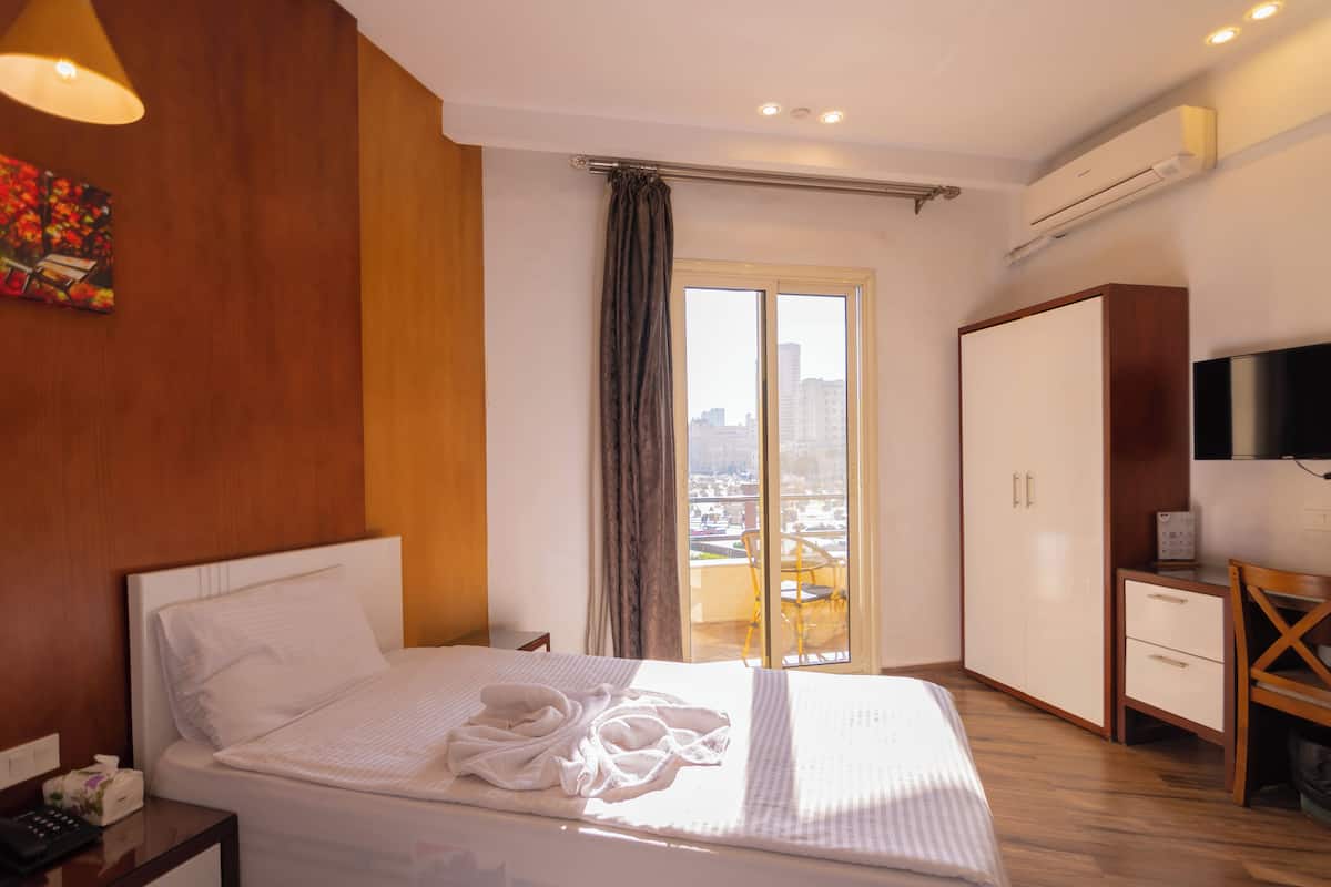 A hotel room with a bed, a desk, a chair, a wardrobe, and a television.