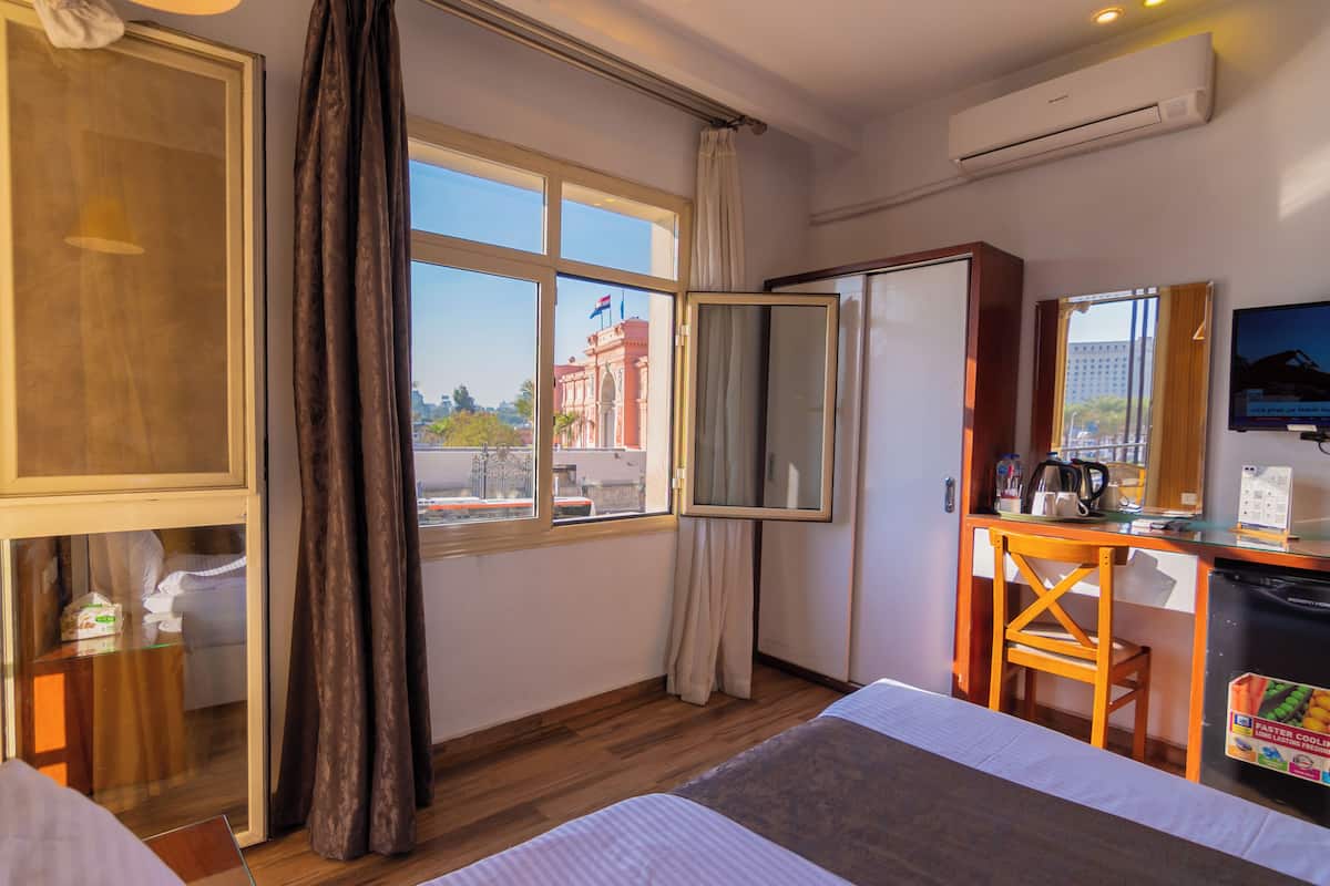 A hotel room with a bed, a desk with a chair, a television, and a window with curtains.