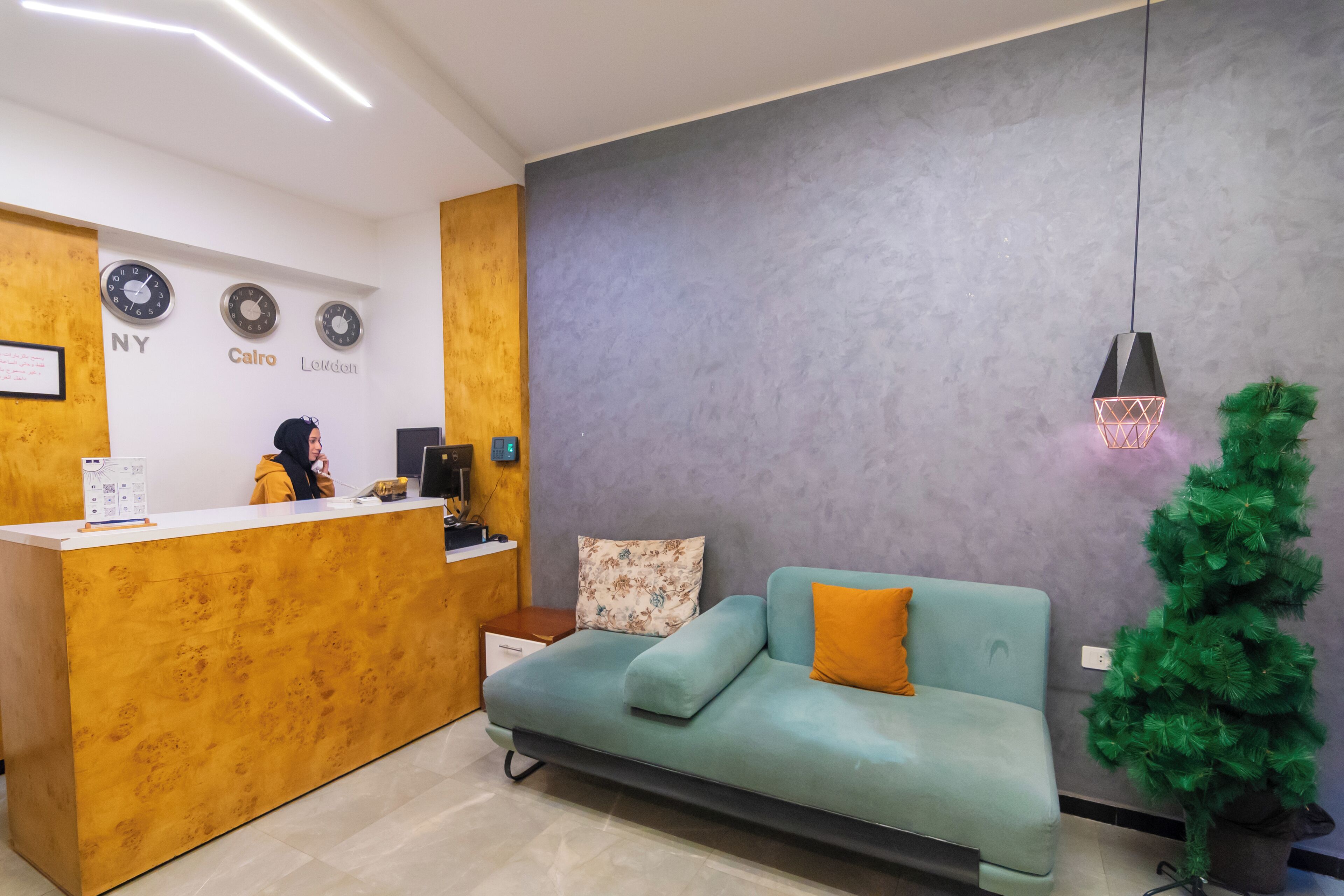 A reception area with a wooden desk, a teal sofa, a green Christmas tree, and clocks displaying different city names.