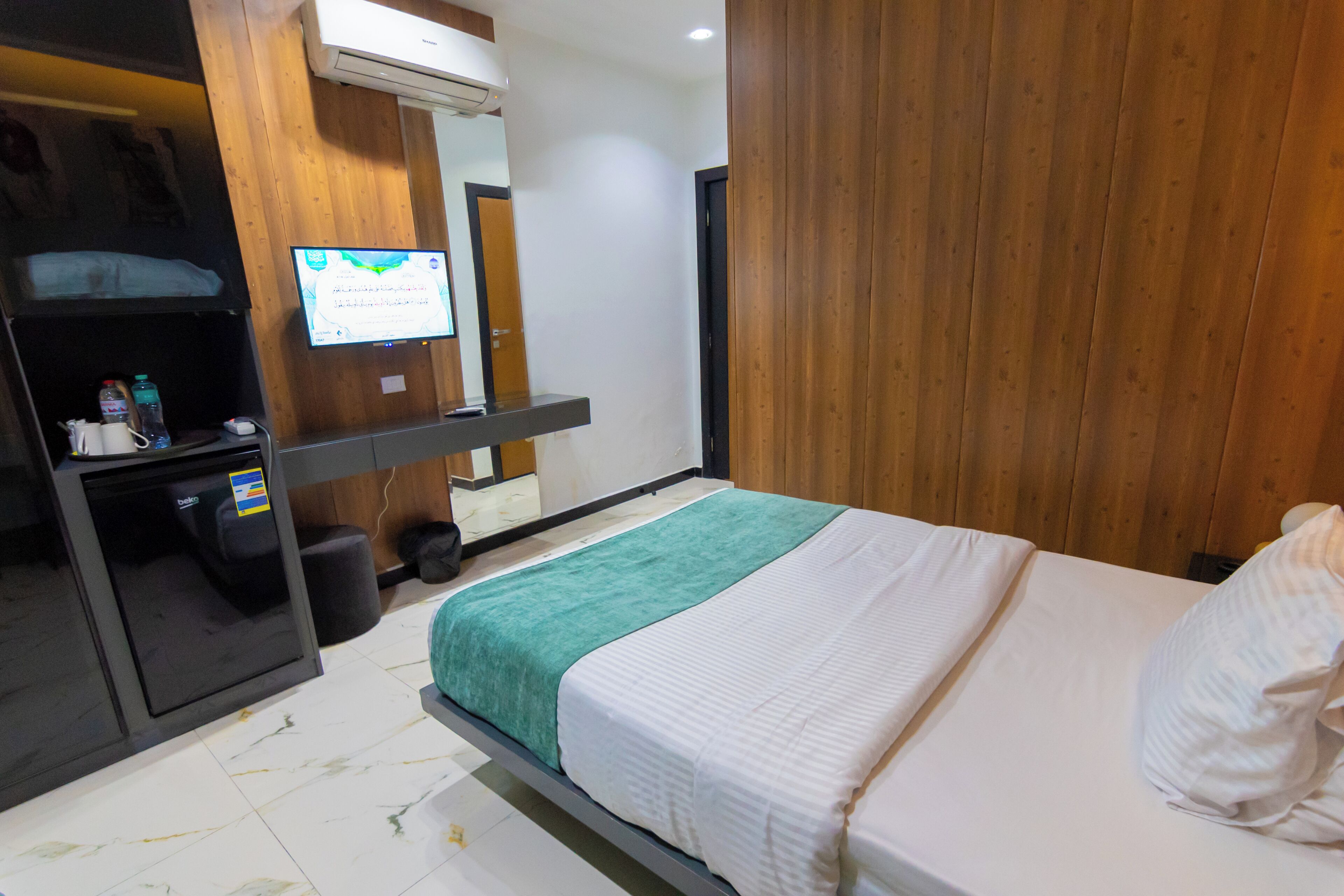 Habitación de hotel con cama, escritorio con computadora, espejo y televisión montada en la pared.