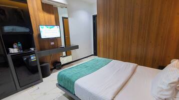 Habitación de hotel con cama, escritorio con computadora, espejo y televisión montada en la pared.