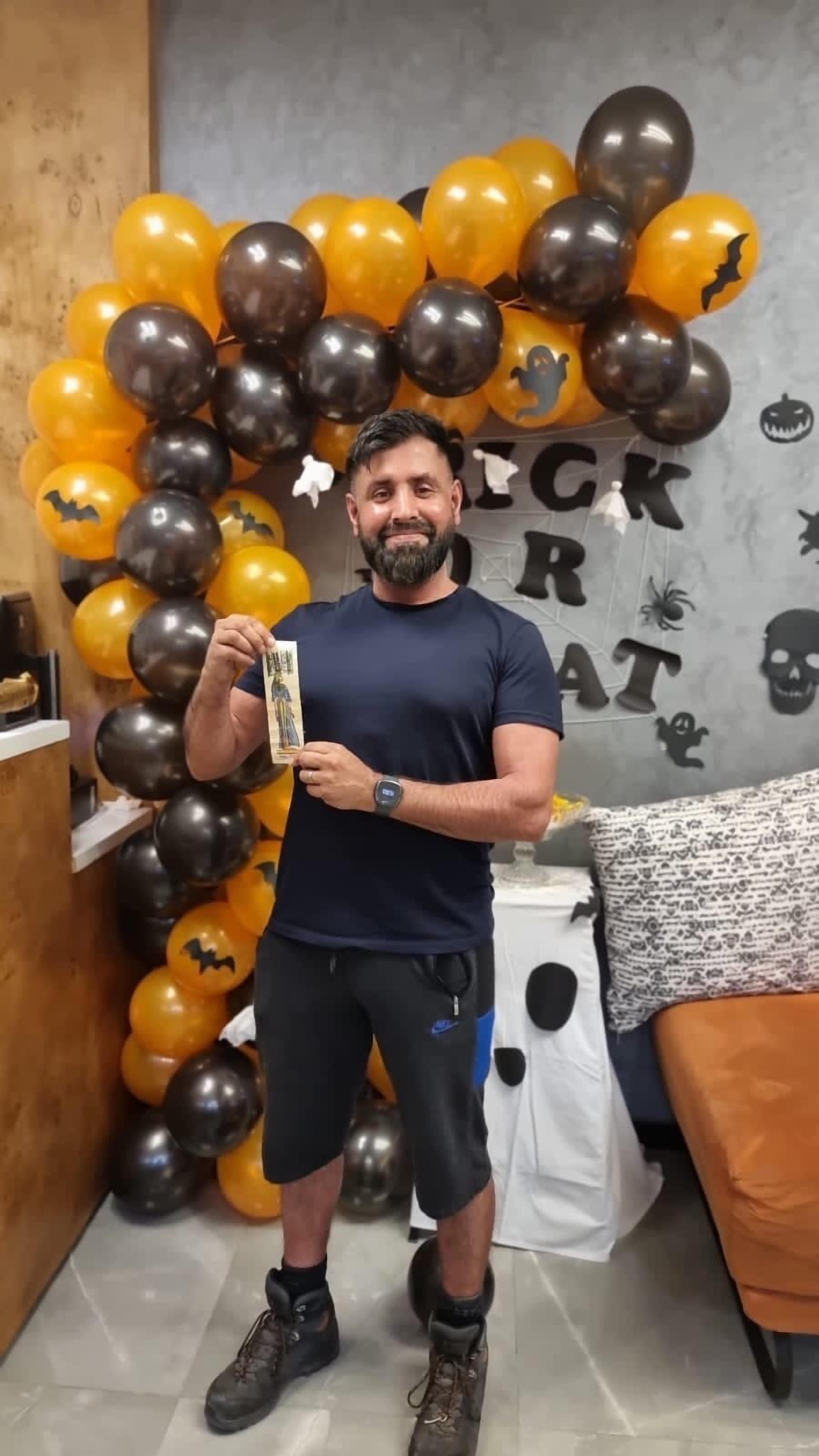 A man holding a booklet in a room decorated with Halloween-themed balloons and wall decorations.