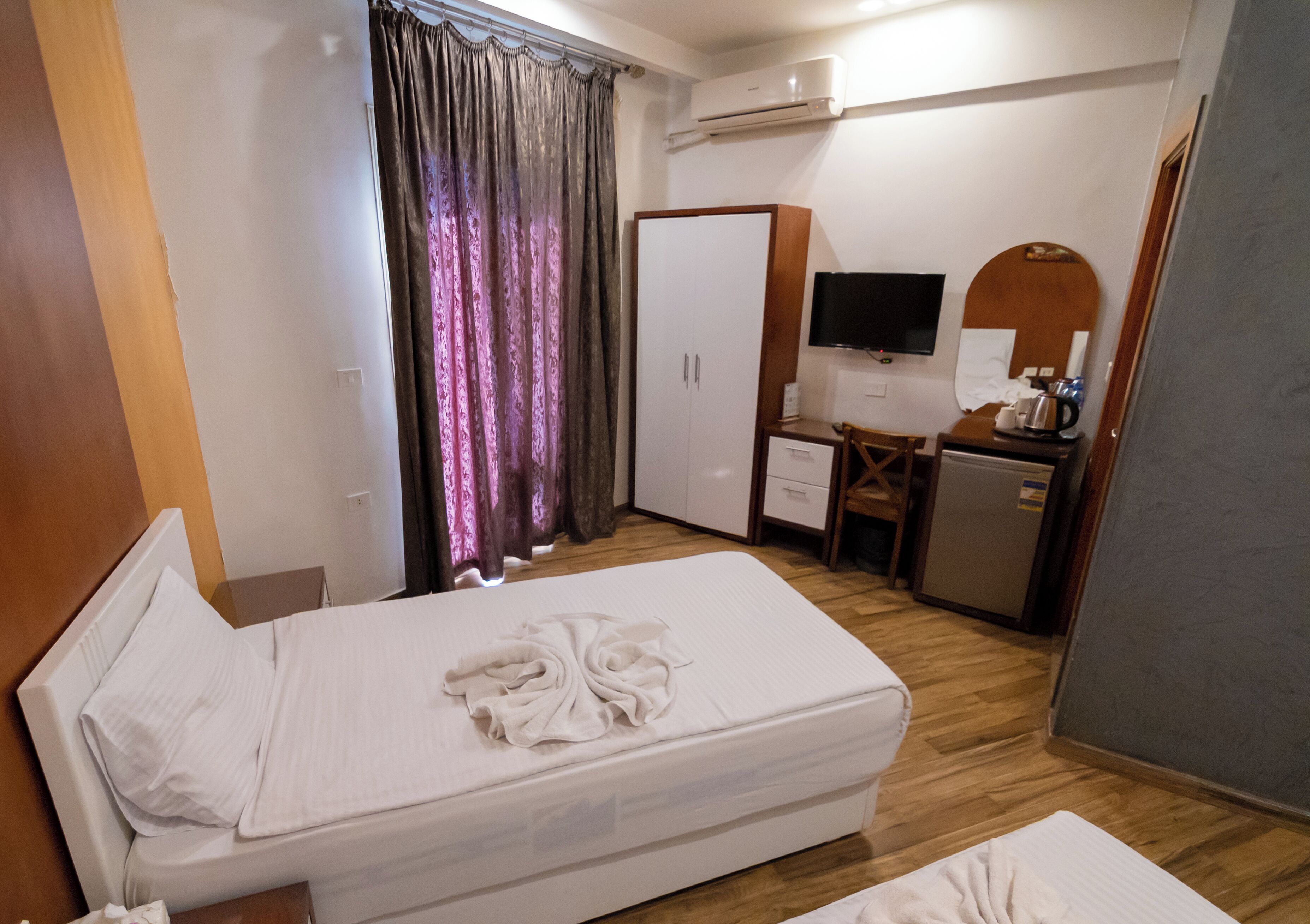 A hotel room with a bed, a desk, a wardrobe, a television, and an air conditioning unit.