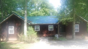 Une cabane rustique avec un toit végétalisé, entourée d’arbres.