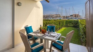 An outdoor dining area with a table set for two, chairs with blue cushions, a bottle of wine, and a bowl of fruit. A view of a marina with boats is visible through the window. - Beautiful apartment for 4 people with WIFI, TV and patio (Cogolin)