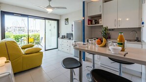 A modern kitchen with white cabinets, a dining area with yellow furniture, and a view of the marina through large glass doors. - Beautiful apartment for 4 people with WIFI, TV and patio (Cogolin)