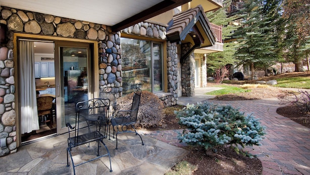 Fachada de piedra con un patio que incluye dos sillas de metal y un pequeño abeto.