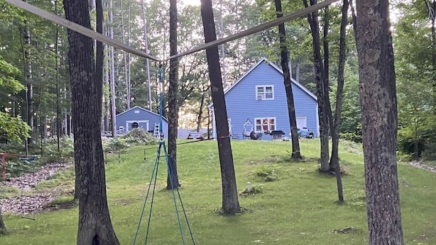 Een schommel in een bebost gebied, met een blauw huis op de achtergrond.