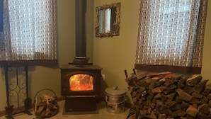 Een gezellige kamer met een houtkachel, een spiegel aan de muur en een kamerbreed gordijn.