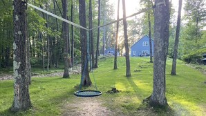 Een schommel in een bebost gebied, met een huis op de achtergrond.