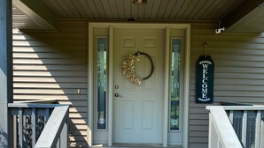 A front porch with a wooden staircase leading to a white door, a welcome mat, and a 'WELCOME' sign. - Beautiful 6 bedroom 3 bath lake front home with view of Lake Nokomis! (Tomahawk)