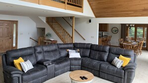 A spacious living area with a large sectional sofa, a wooden staircase, and a kitchen in the background. - Beautiful 6 bedroom 3 bath lake front home with view of Lake Nokomis! (Tomahawk)