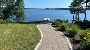 A paved pathway leading to a lake with a covered area, surrounded by grass and plants. - Beautiful 6 bedroom 3 bath lake front home with view of Lake Nokomis! (Tomahawk)