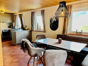 Moderni keittiö, jossa on ruokailutila, ja tilaan kuuluu pöytä, tuoleja ja penkki.