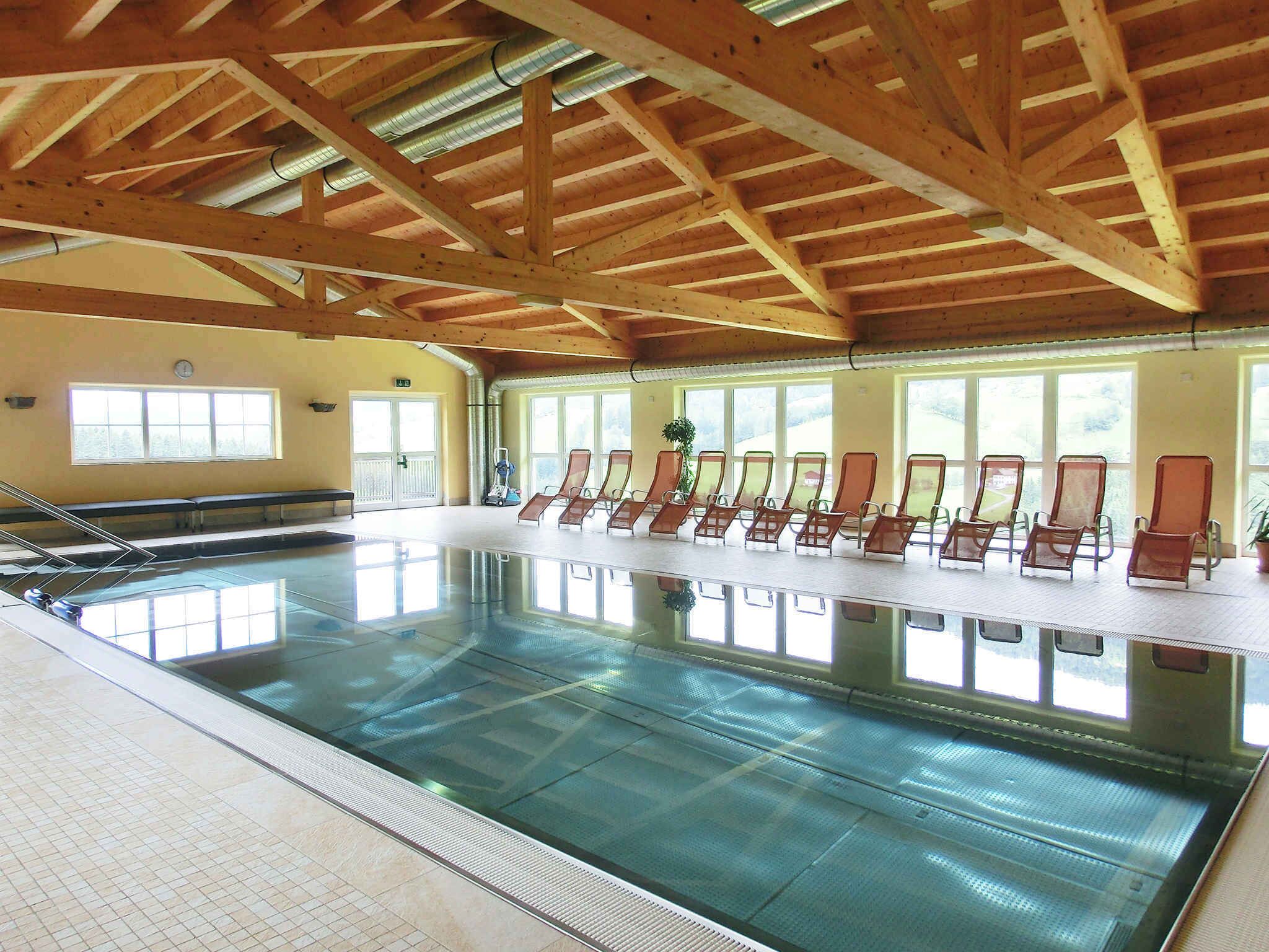 An indoor swimming pool with a wooden ceiling and sunlit windows.