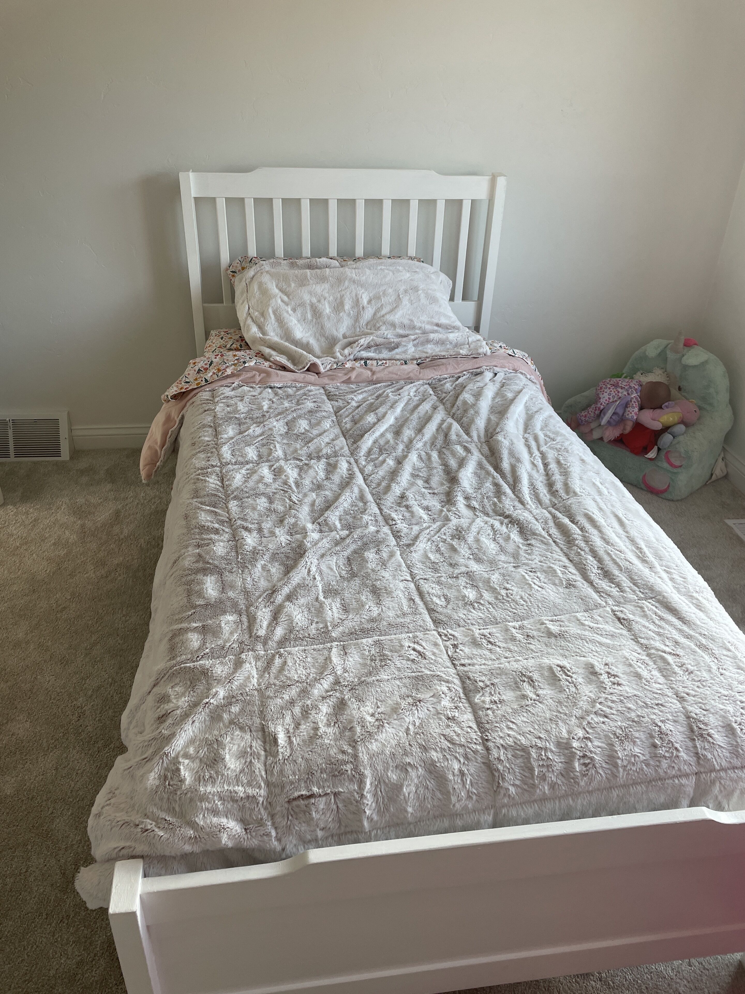 Ein ordentlich bezogenes Bett mit einem weißen Kopfteil, einer gemusterten Decke und einem rosafarbenen Kissen.