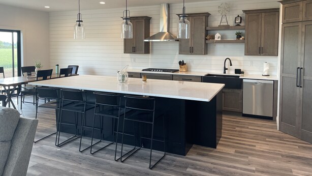 Een moderne keuken met een groot eiland, hangende lampen en houten kastjes.