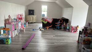 Een ruime kamer met hoge plafonds en houten vloeren, voorzien van diverse kinderspeelgoed en speeltoestellen.