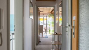 A corridor with a wooden ceiling, a metal shelf, and a door leading to an outdoor area with a table and chairs. - Apartment "Säntisblick" with Beautiful View of Lake Constance and the Alps (Daisendorf)