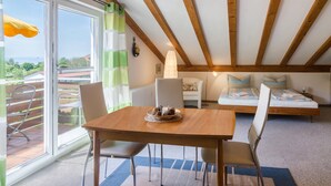 A room with a wooden ceiling, a dining table with chairs, a sofa, and a view through large windows. - Apartment "Säntisblick" with Beautiful View of Lake Constance and the Alps (Daisendorf)