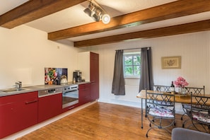 Una cocina con armarios rojos, una mesa de comedor de madera y una ventana con cortinas.