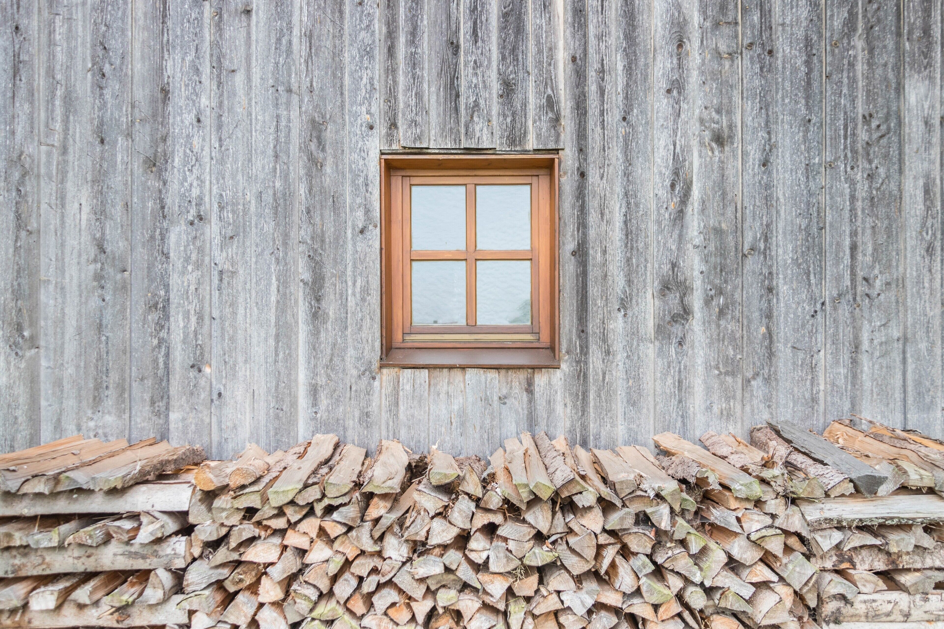Un mur en bois rustique, avec une fenêtre et une pile de bois de chauffage.