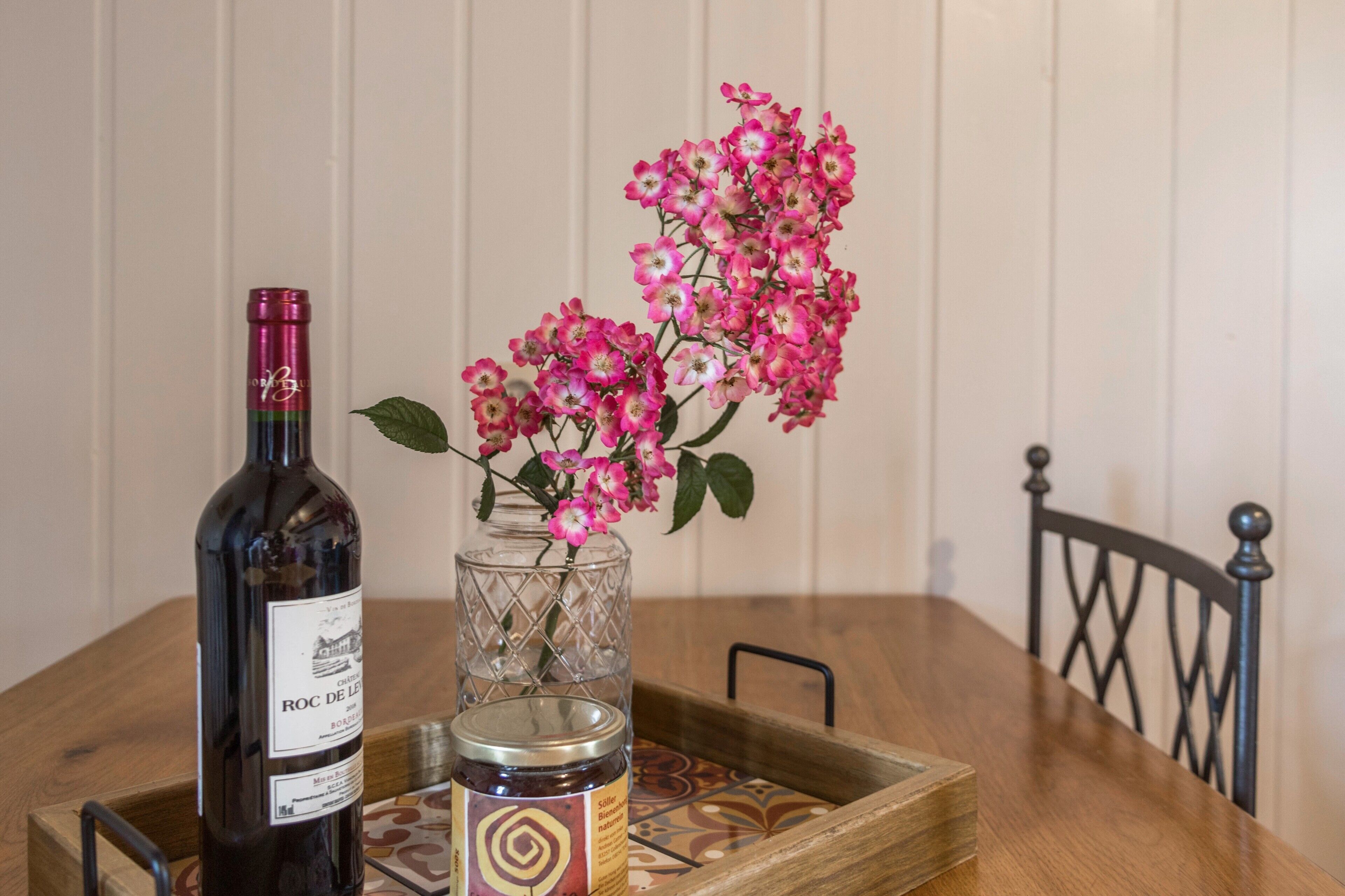 En flaska vin, ett glas med sylt och rosa blommor på ett träbord.