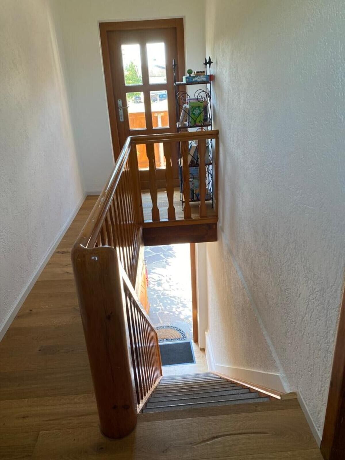 A wooden staircase with a handrail, a door leading outside, and a metal rack with items on the landing.