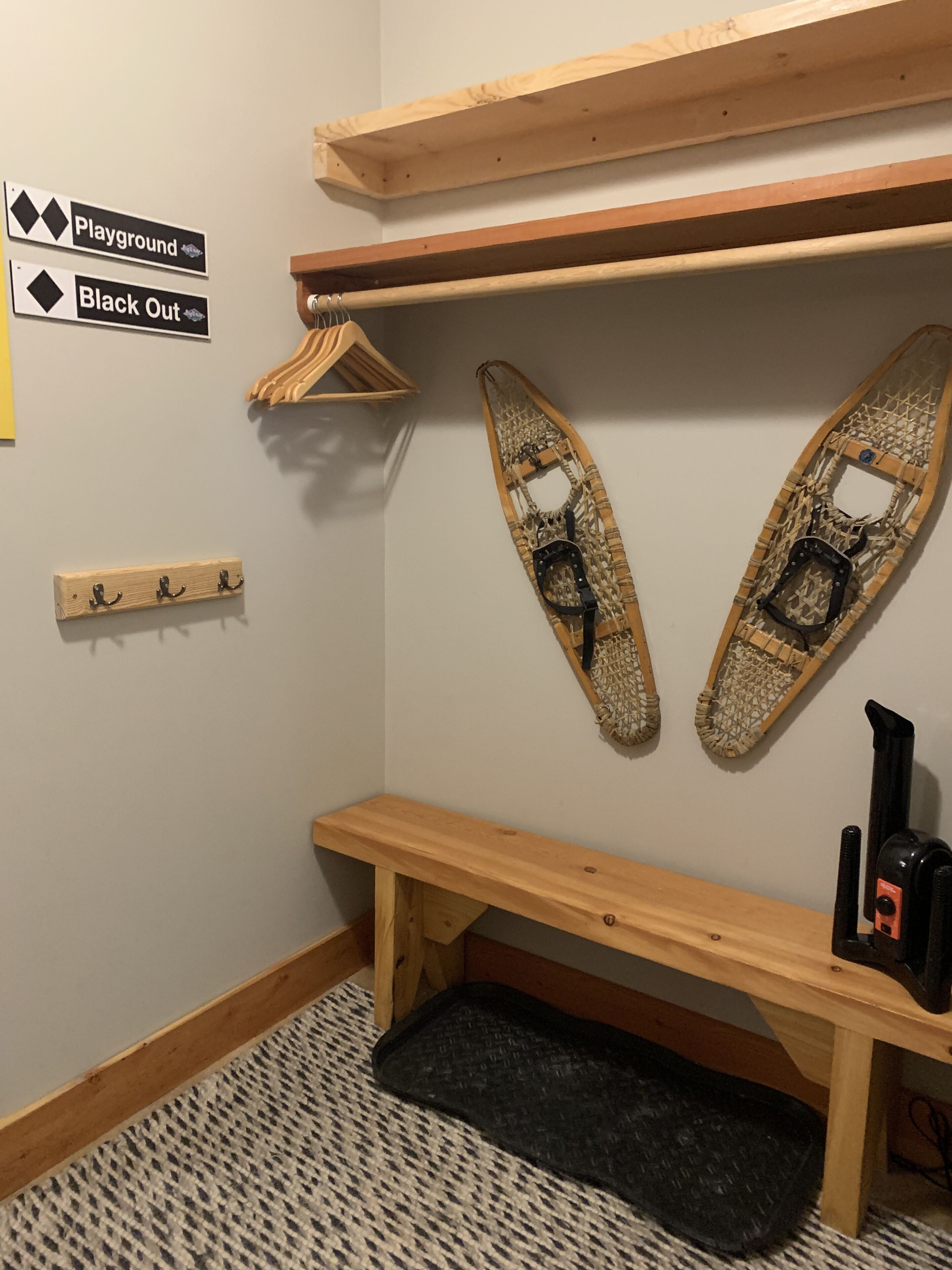 A corner of a room with a wooden bench, a wall-mounted rack, and a pair of skis.