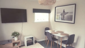 A compact living space with a flat-screen TV, a dining area with a table and chairs, a small plant, and a framed picture on the wall.