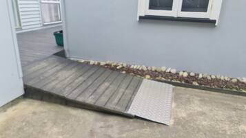 Un patio de concreto con una rampa de madera y una barandilla metálica que conduce a una puerta.