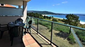 Un balcon avec une table et des chaises donnant sur une plage et des montagnes.