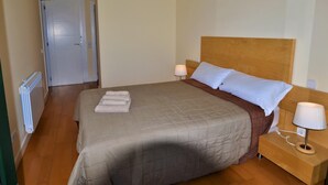 Un lit bien fait, avec une tête de lit en bois, deux lampes de chevet et une serviette pliée posée sur le lit.