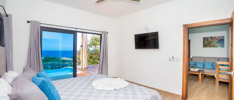 Ein Schlafzimmer mit Bett, Deckenventilator, Fernseher und Blick ins Freie.