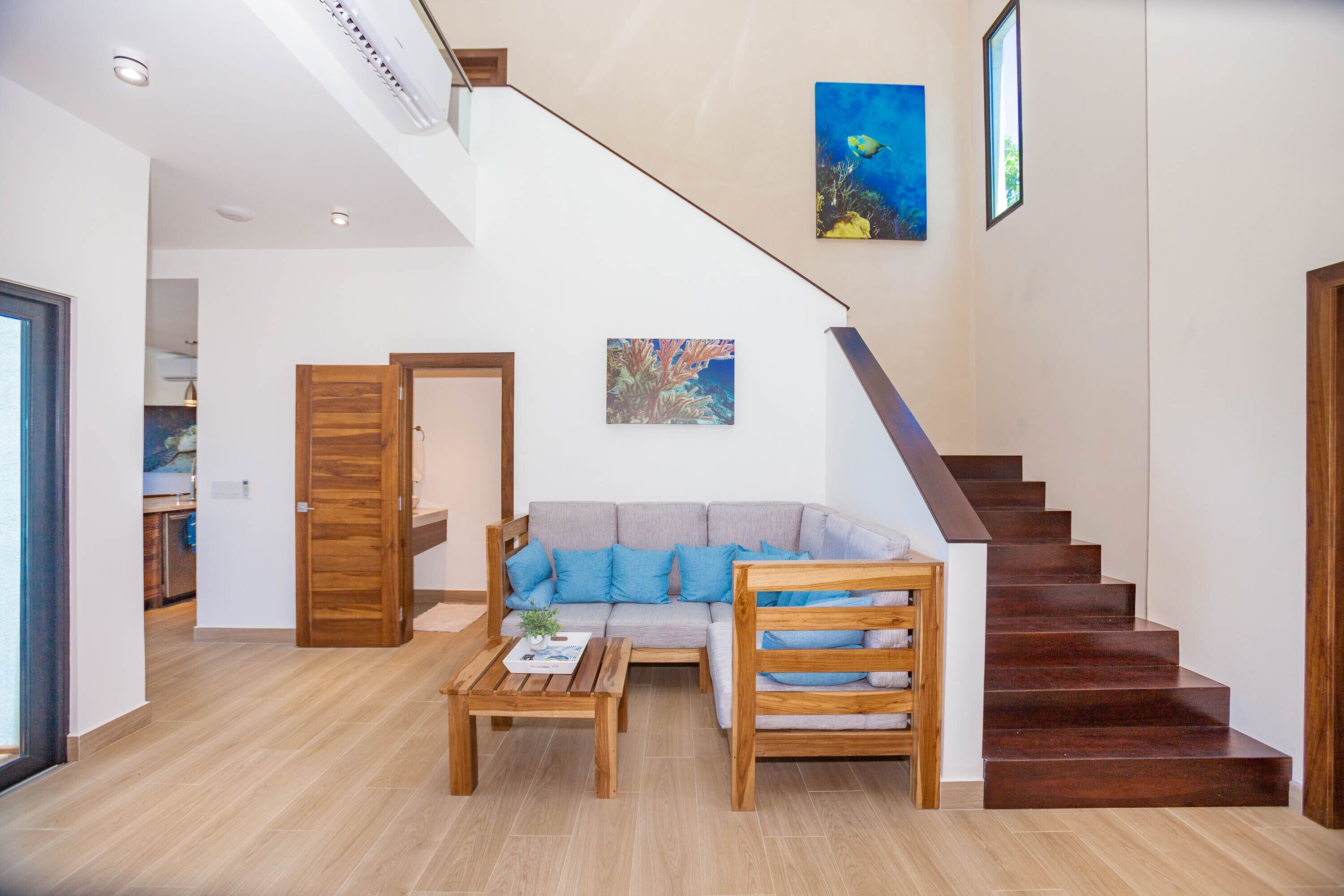A modern living room with a staircase, wooden furniture, and two paintings.