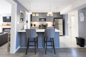 A modern kitchen with grey cabinets, stainless steel appliances, and two bar stools. - Modern House| Walk to the Falls   (Niagara Falls)
