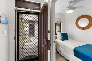 A hotel room with a bed, a ceiling fan, a wall-mounted mirror, and a door with a mesh screen.