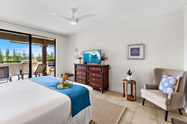 A hotel room with a bed, a television, a dresser, a chair, and a view of the outdoors.